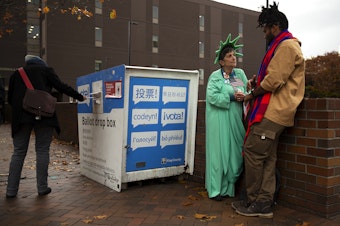 caption: Patti Gorman, dressed as lady liberty, talks with her former Seattle Central student, Afrikaan Sahra, right, as voters cast their ballots on Tuesday, Nov. 5, 2024, outside of Seattle Central College in Capitol Hill. Sahra was voting for the first time after receiving U.S. citizenship. 