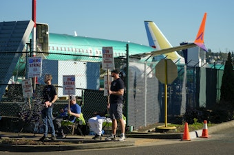 caption: Boeing 737 Max aircrafts are seen behind fences as Boeing employees work the picket line while striking Tuesday, Sept. 24, 2024, next to the company's facilities in Renton, Wash. 