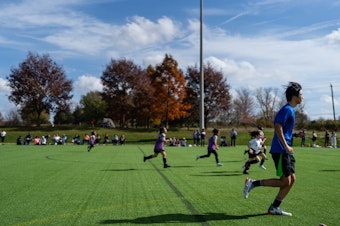 caption: Jason Kim a new referee being mentored by Peter Guthrie runs to follow a play during a youth soccer match.