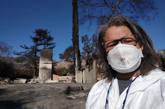 caption: KUOW Morning Edition host Angela King dons PPE in front of what remains of aunt’s home in Altadena. 