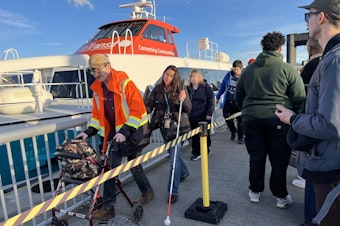 caption: Passengers disembarking from one of Kitsap Transit's passenger-only ferries while others wait to embark in February 2024.