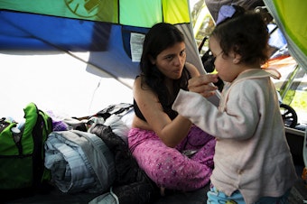 caption: Brithany, of Venezuela, feeds her 1.5-year-old daughter inside their tent on Wednesday, May 1, 2024, at Powell Barnett Park in Seattle. Brithany says their family is in desperate need of clothing. 