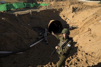 caption: Israeli military spokesman Rear Adm. Daniel Hagari stands at the opening to a tunnel near the border with Israel on Dec. 15, 2023, northern Gaza Strip. The Israeli military said this was the largest tunnel they'd found yet in Gaza.