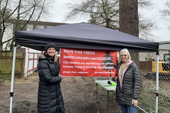 caption: Lake City residents April Cowgill, left, and Carlen Luke in front of the Douglas Fir slated for removal by developers in January 2025.