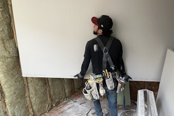 caption: A worker installs sheetrock in a South Seattle townhome in February, 2025.