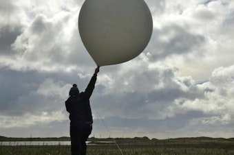 caption: National Weather Service meteorologist William Wells raises a weather balloon for launch on St. Paul Island, Alaska, in October 2015.