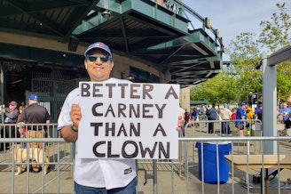 caption: A Toronto Blue Jays fan waives a sign that reads, "Better A Carney Than A Clown" in Seattle on Friday, May 9, 2025.