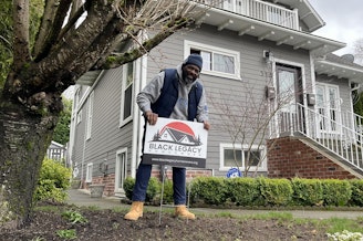 caption: Chukundi Salisbury places a new sign in front of a home owned by a member of the Black Legacy Homeowners' group in Seattle's Central District.