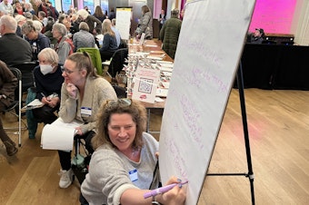 caption: Sarah Burdell takes notes for her group at Rep. Pramila Jayapal's Resistance Lab in Seattle on March 20, 2025. 