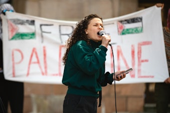 caption: Bissan Barghouti, an organizer with Nidal Seattle and the Masar Badil, speaks to crowd rallying outside of Gerberding Hall on Thursday, May 8, 2025, on the University of Washington campus in Seattle. 