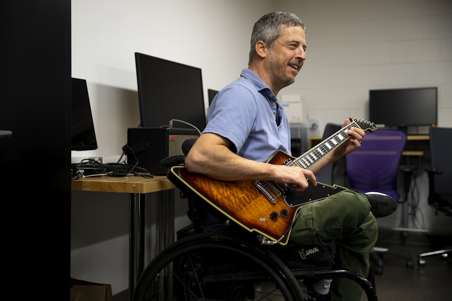 caption: Jon Schlueter, who became injured in a diving accident, plays guitar on Monday, April 15, 2024, at Wallace Hall on the University of Washington campus in Seattle. Schlueter gained increased mobility in his left hand after participating in a University of Washington study using noninvasive transcutaneous spinal cord stimulation.